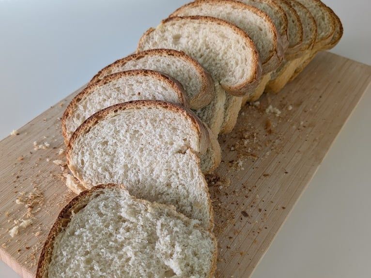 Pan de molde casero cortado en rebanadas y dispuesto en abanico sobre una tabla de madera, con corteza dorada y miga clara y esponjosa.