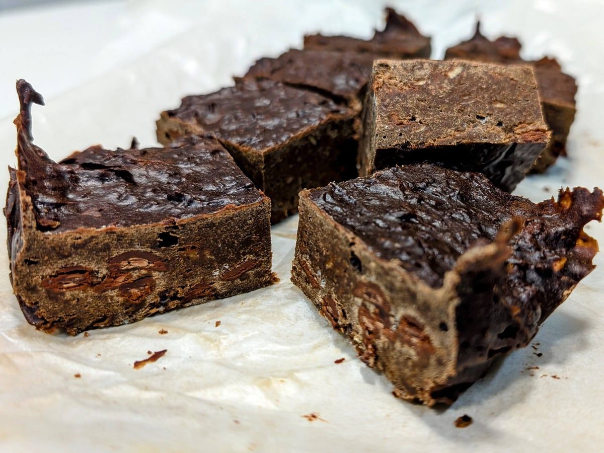 Trozos de brownie oscuros y muy densos, con trozos de chocolate visibles en el corte, apoyados sobre papel de hornear.